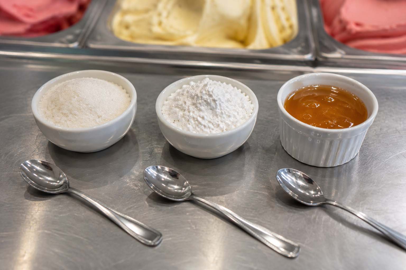 Diferentes tipos de açúcar (sacarose, dextrose, mel) em potes separados sobre bancada de sorveteria